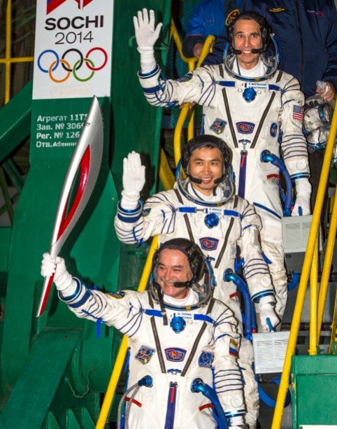 Sochi 2014 Expedition 38 Soyuz Commander Mikhail Tyurin, holding the Olympic torch, and Flight Engineers Koichi Wakata and Rick Mastracchio wave farewell prior to boarding the Soyuz TMA-11M rocket for launch. PHOTO: NASA