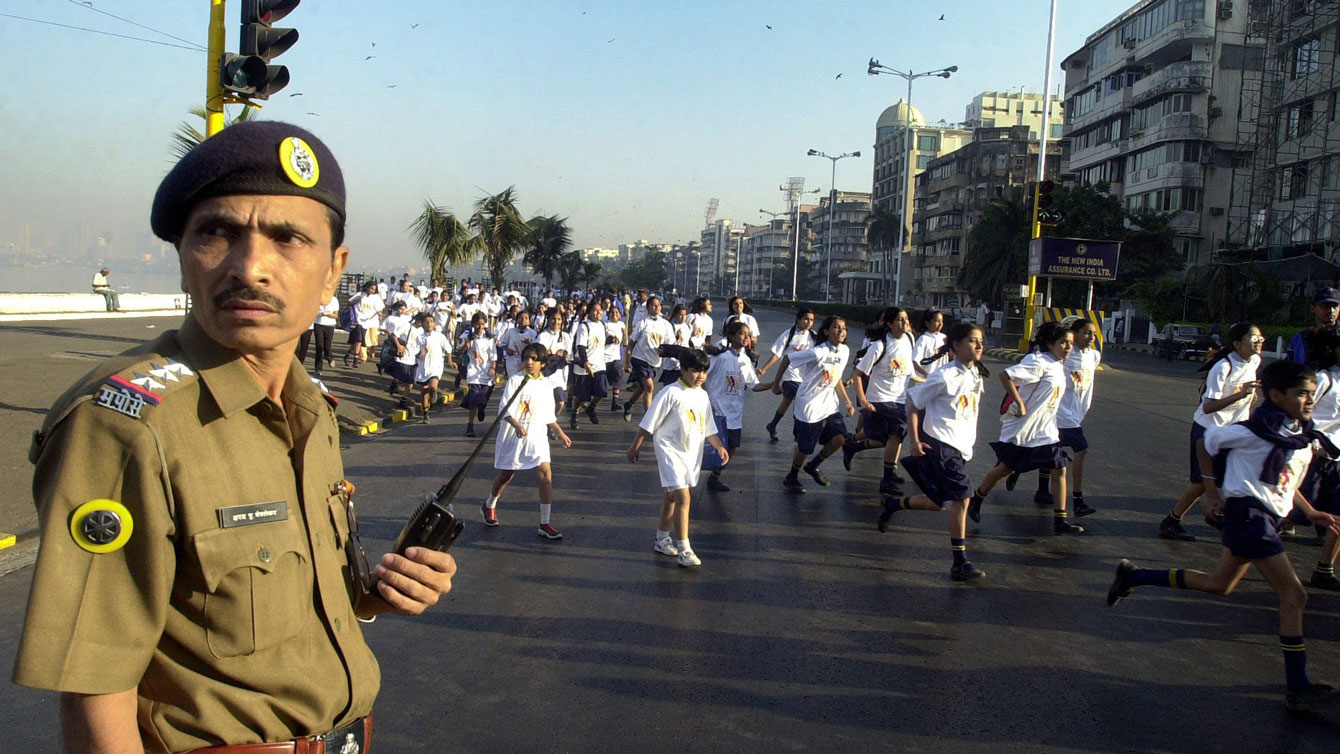A police officer stands on guard as children take part in an international Terry Fox Run, Bombay, India in 2004.