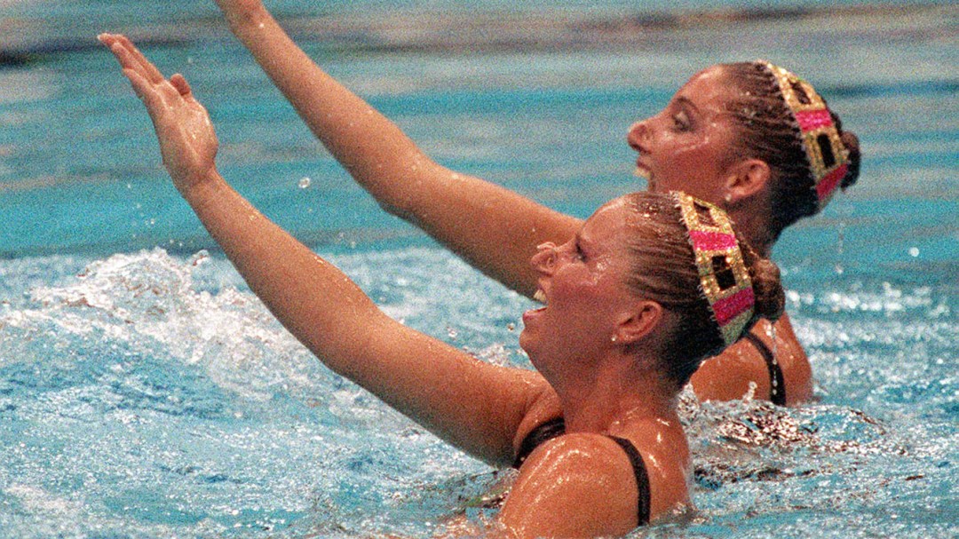 Carolyn Waldo and Michelle Cameron each raise an arm in their synchronized swimming routine
