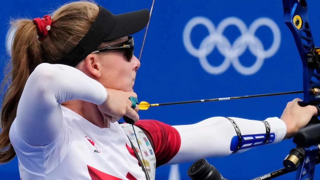 Vrginie Chenier pulls back on her bow with the Olympic rings in the background