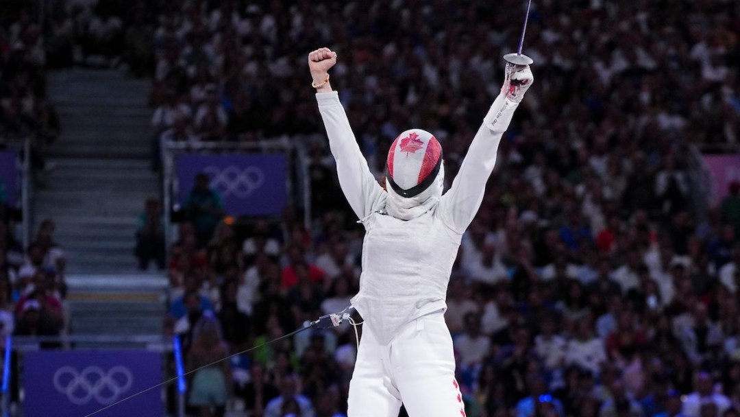 Eleanor Harvey raises both hands in celebration while wearing a Canadian flag mask