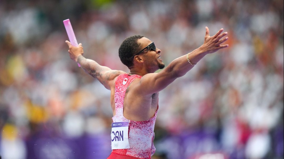 Andre De Grasse raises his arms in celebration while holding a baton