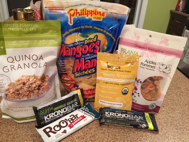 Assorted snacks, including dried mangos, dried apple, quinoa granola for breakfast, almonds, protein bars.