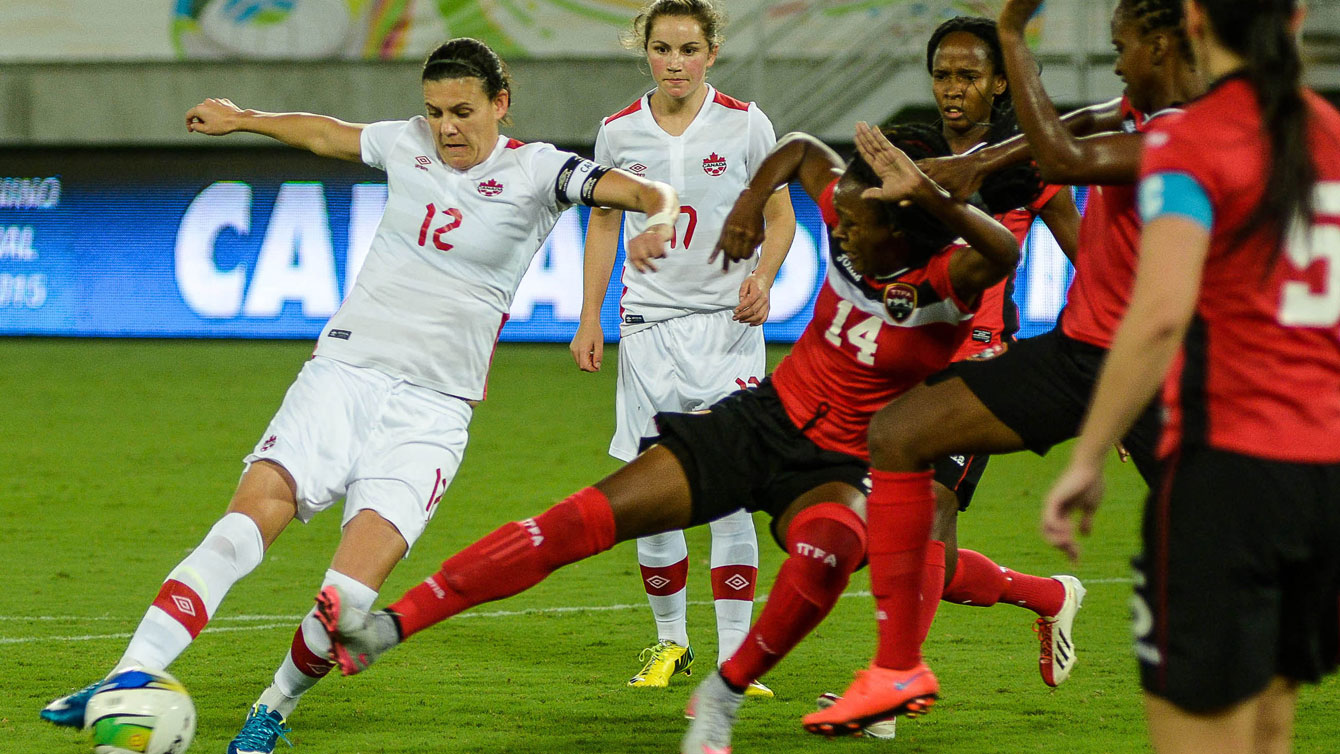 Christine Sinclair (left, in white) sets up to shoot against Trinidad and Tobago on December 13, 2015 at the invitational tournament in Natal. Sinclair scored at the 85th minute to tie Mia Hamm with 158 career goals for second on the all-time list (Photo: Vlademir Alexandre/Allsports). 