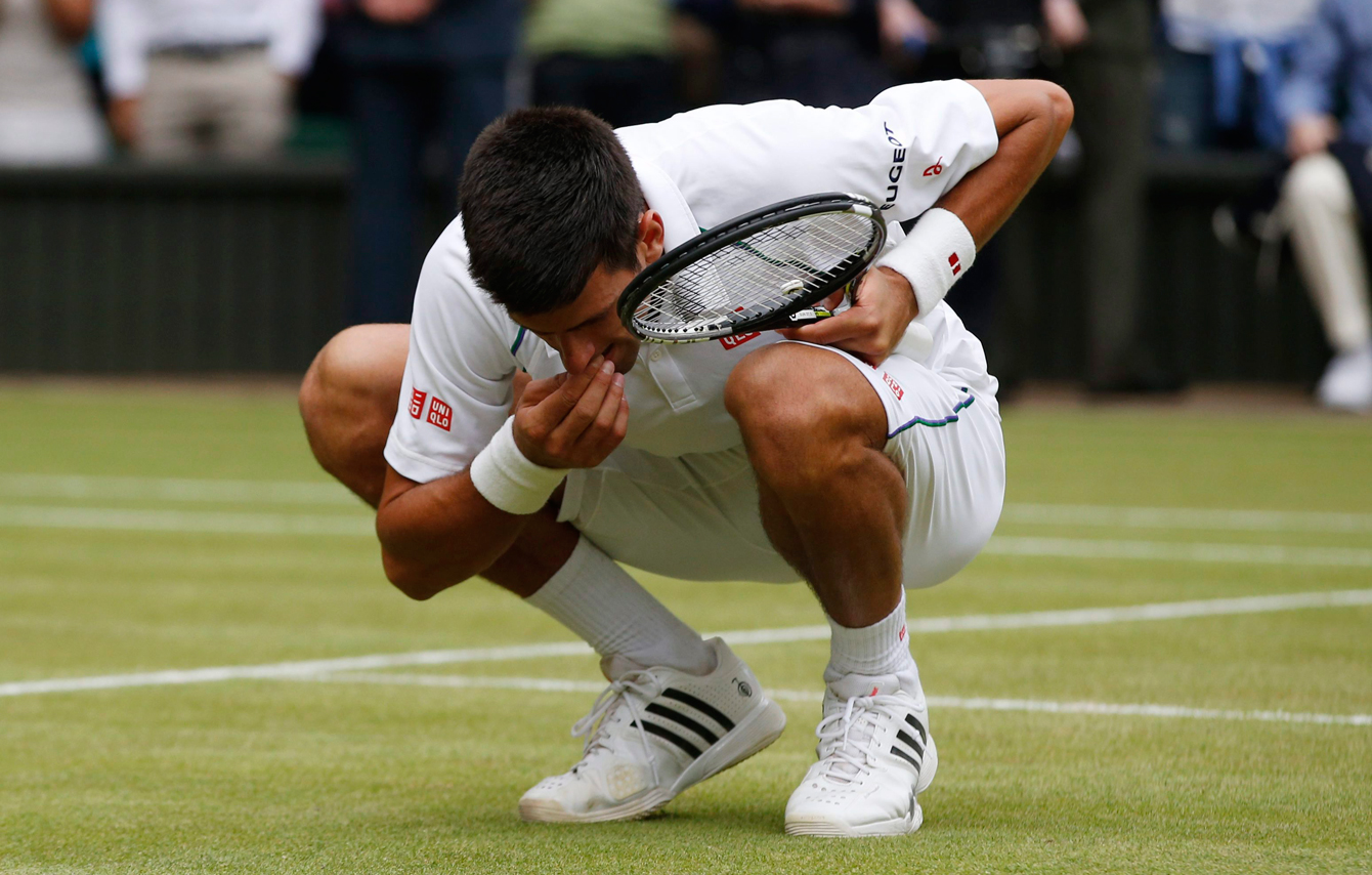 Novak Djokovic eats the grass at Centre Court after winning the men's title against Roger Federer on July 12, 2015. 