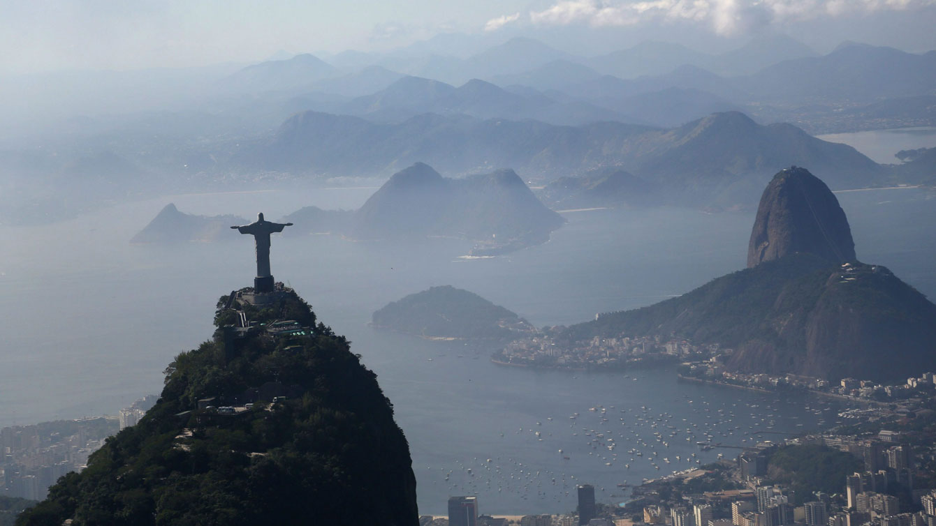 Christ the Redeemer statue stands above Rio de Janeiro, Brazil. Sugarloaf Mountain is at right.