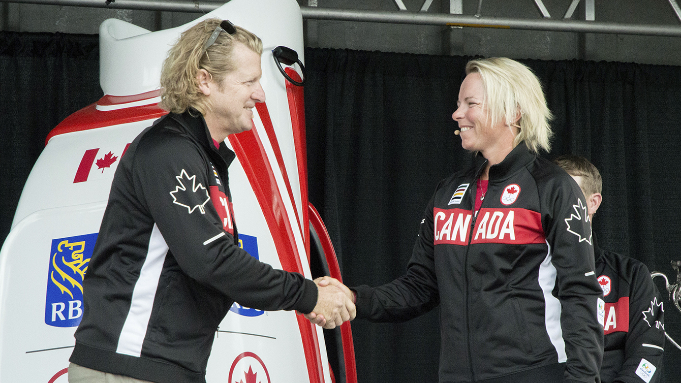 Curt Harnett, Team Canada's chef de mission, gives golfer Alena Sharp her Olympic jacket at the Glen Abbey Golf Club on July 19, 2016. (Tavia Bakowski/COC)
