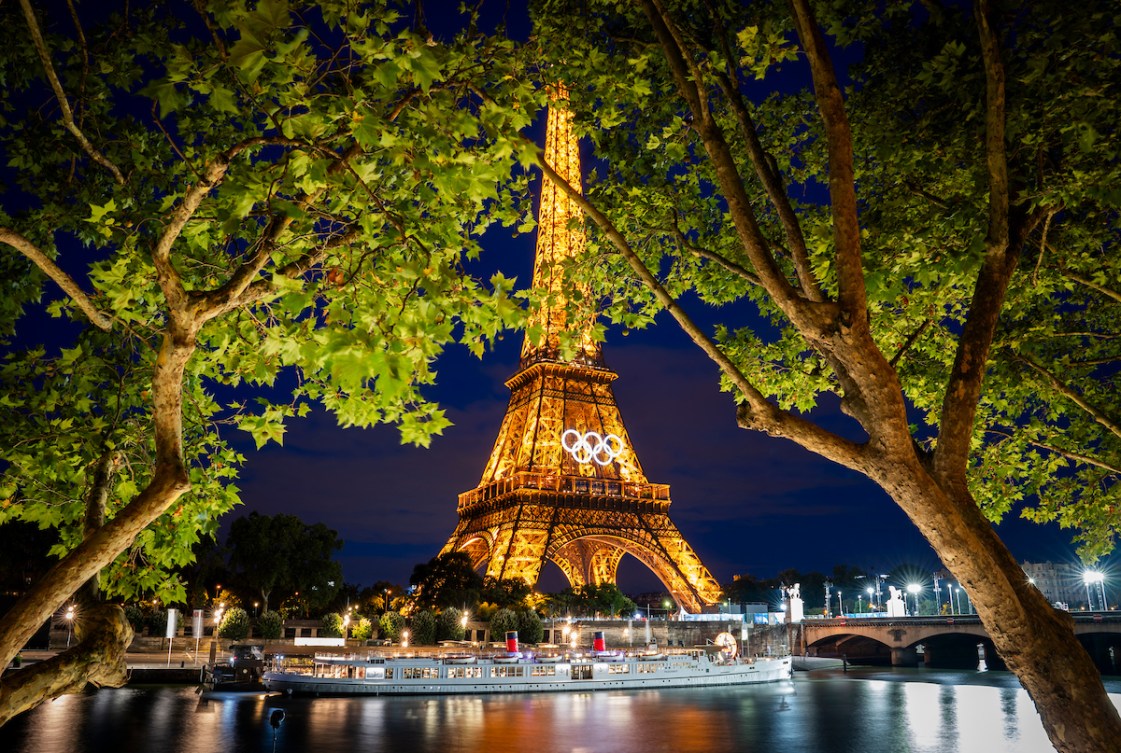 The Eiffel Tower lit up at night while a boat floats  in front of it 
along the Seine