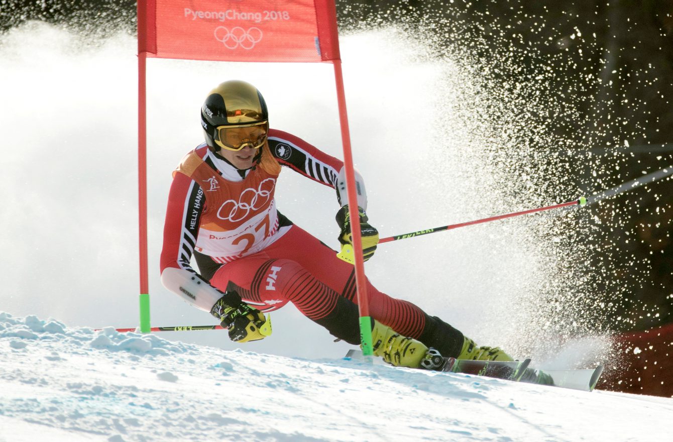 Erik Read mid-competition in the giant slalom at PyeongChang 2018. He is wearing a red, orange and white suit, and a chrome yellow helmet with matching goggles.