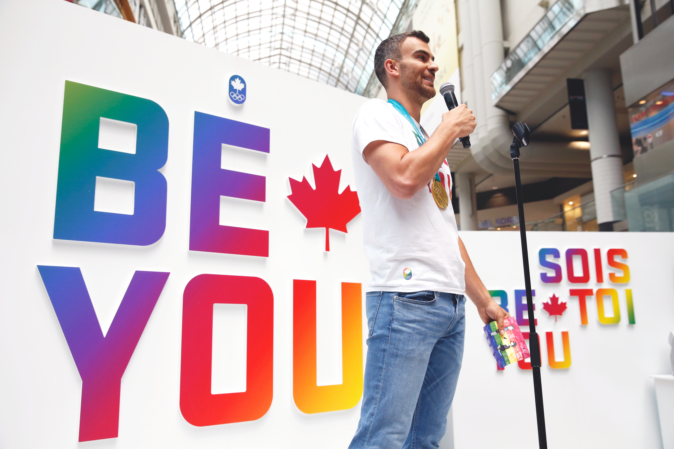 Eric Radford stands in front of Be You sign and speaks to the crowd.
