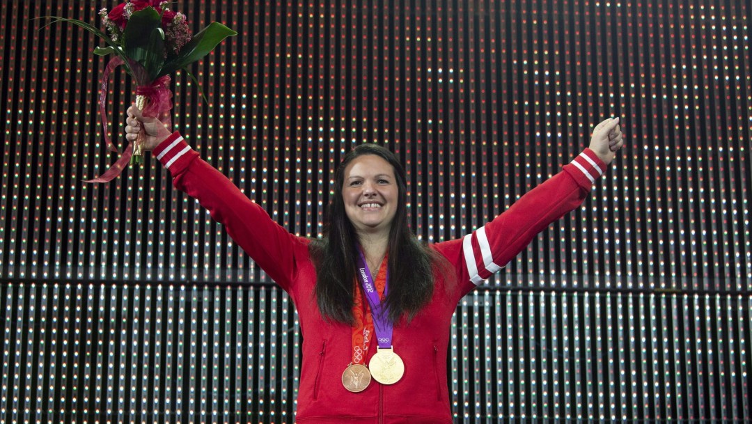 Christine Girard raises her arms in celebration while wearing two medals