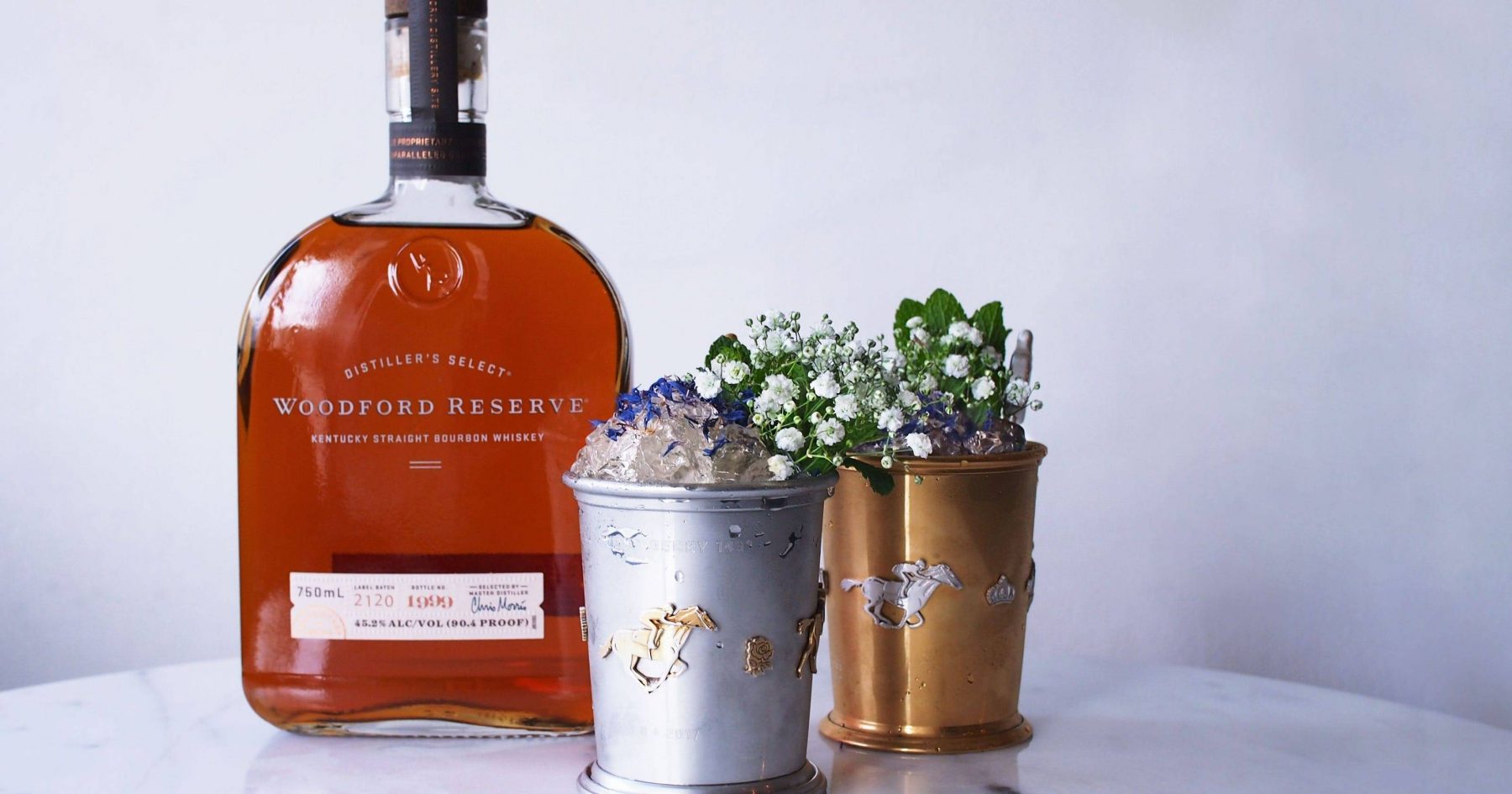 Mint Julep cup in a gold and silver cup with a bottle of Woodford Reserve behind