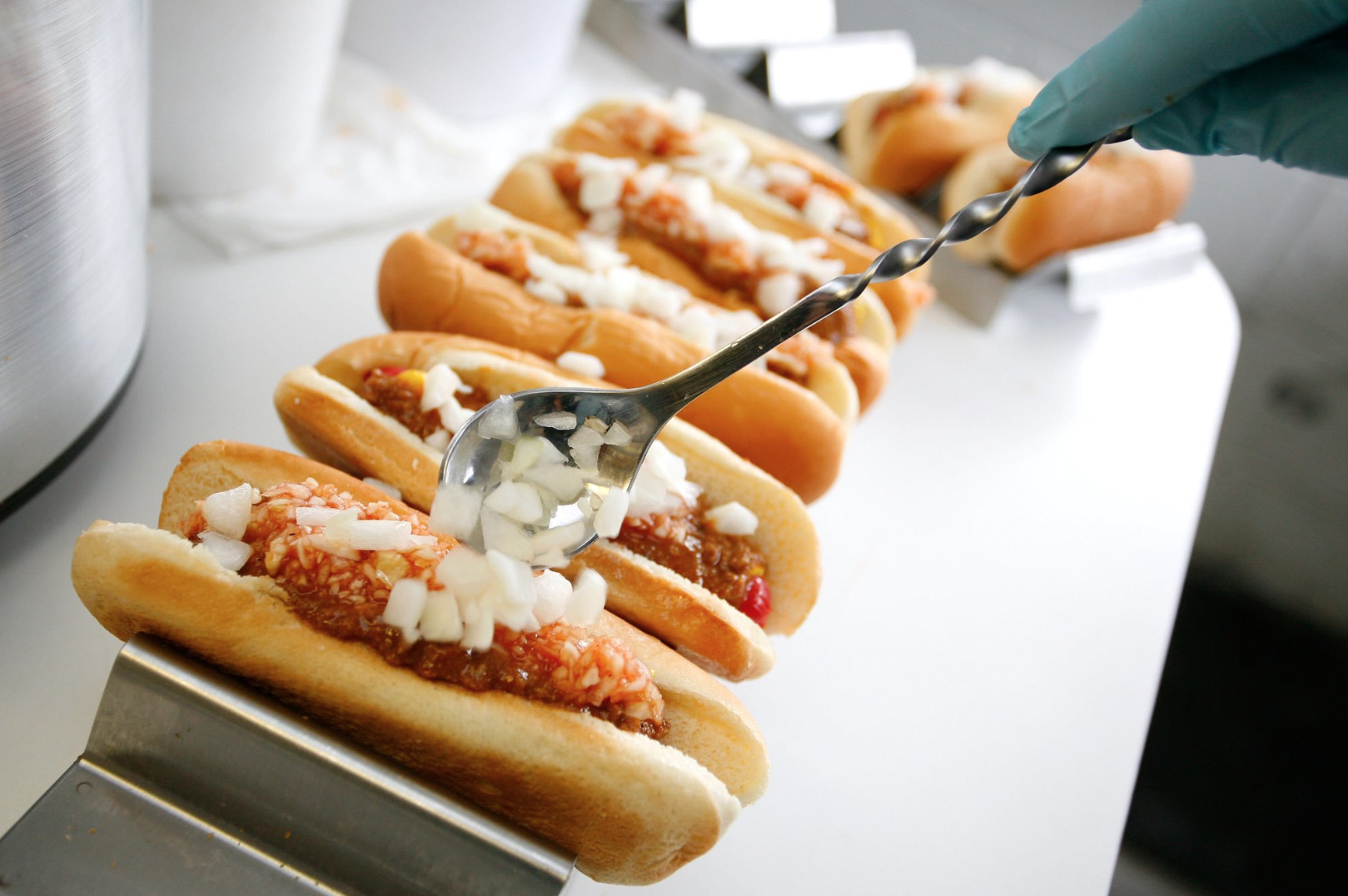Hotdogs lined up with someone placing onions on them