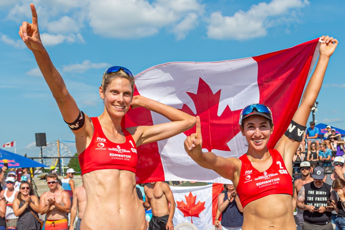 Sarah Pavan and Melissa Humana-Paredes hold the Canadian flag behind them and hold up their index finger to signal they are number one.