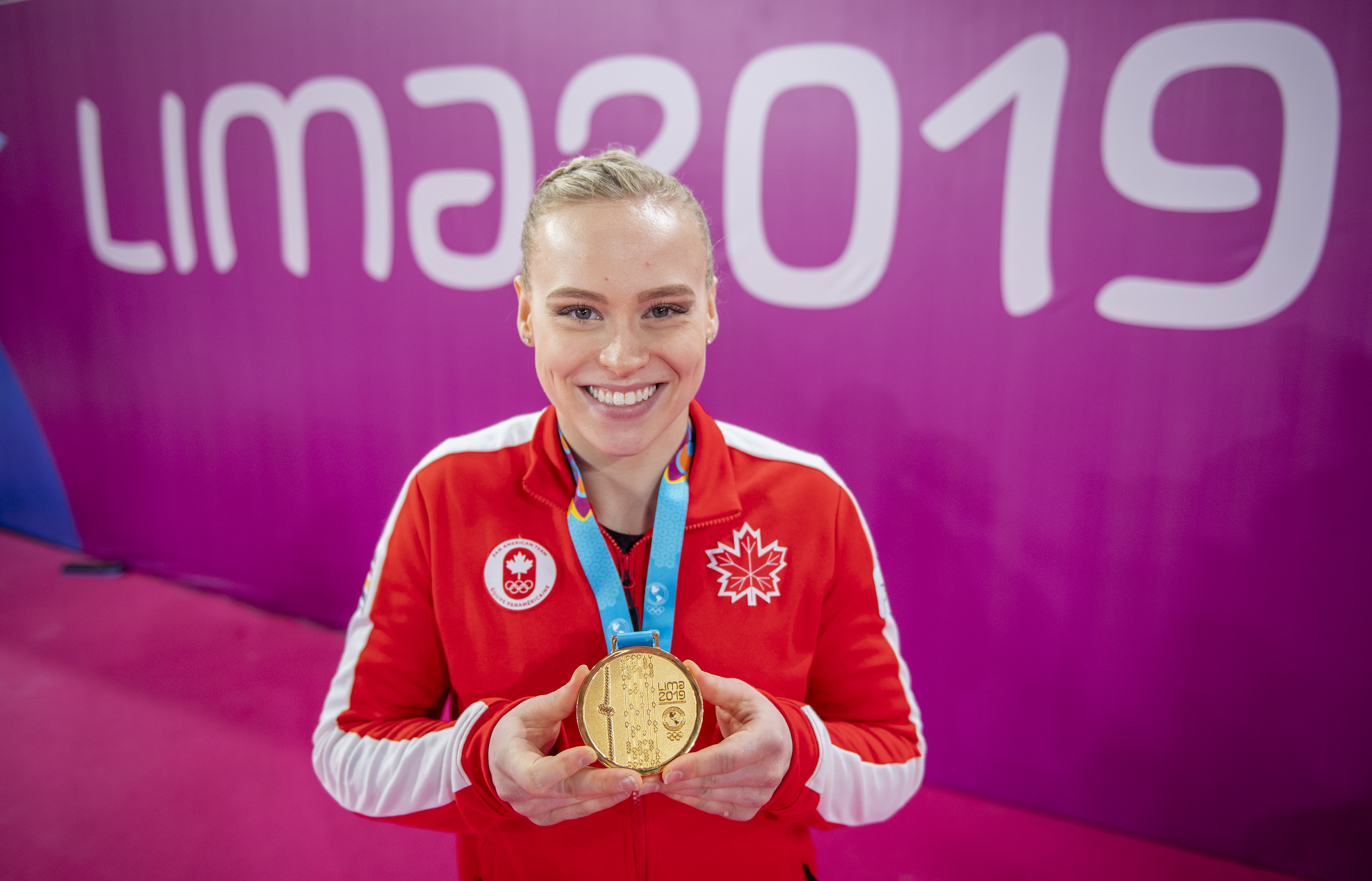 Athlete poses with her gold medal in front of Lima 2019 sign