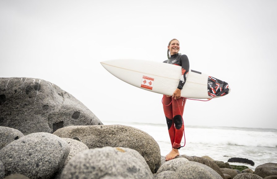 woman stands on rocks with a surf board