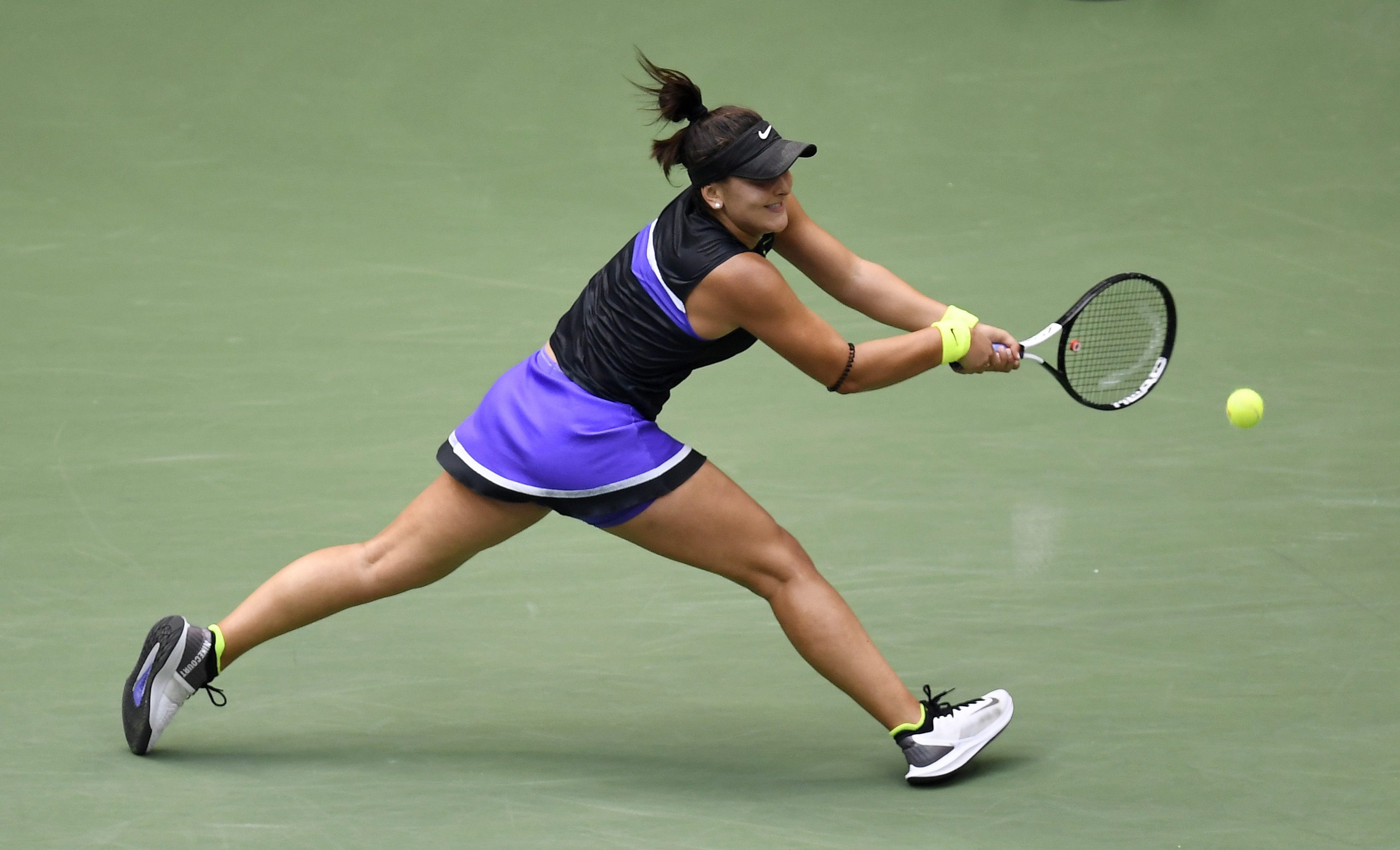 Bianca Andreescu returns a shot. She is wearing a purple and black outfit.