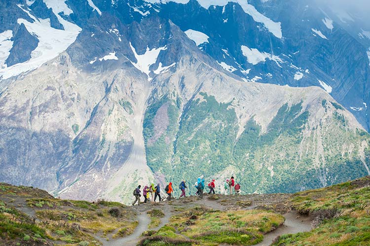 hikers walk along the base of a mountain.