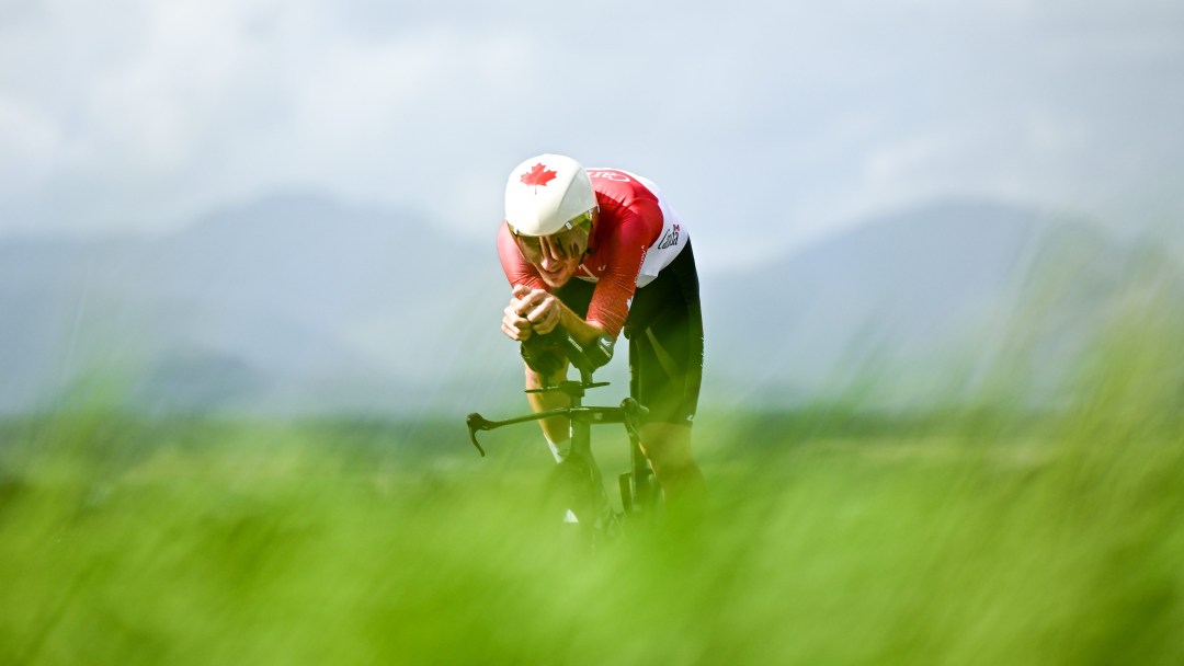 Derek Gee hunches over his road bike in a green landscape