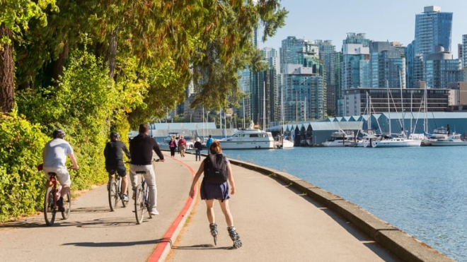 Roller bladers and cyclists on bike path looking out on to the city by the water in Vancouver on a sunny day