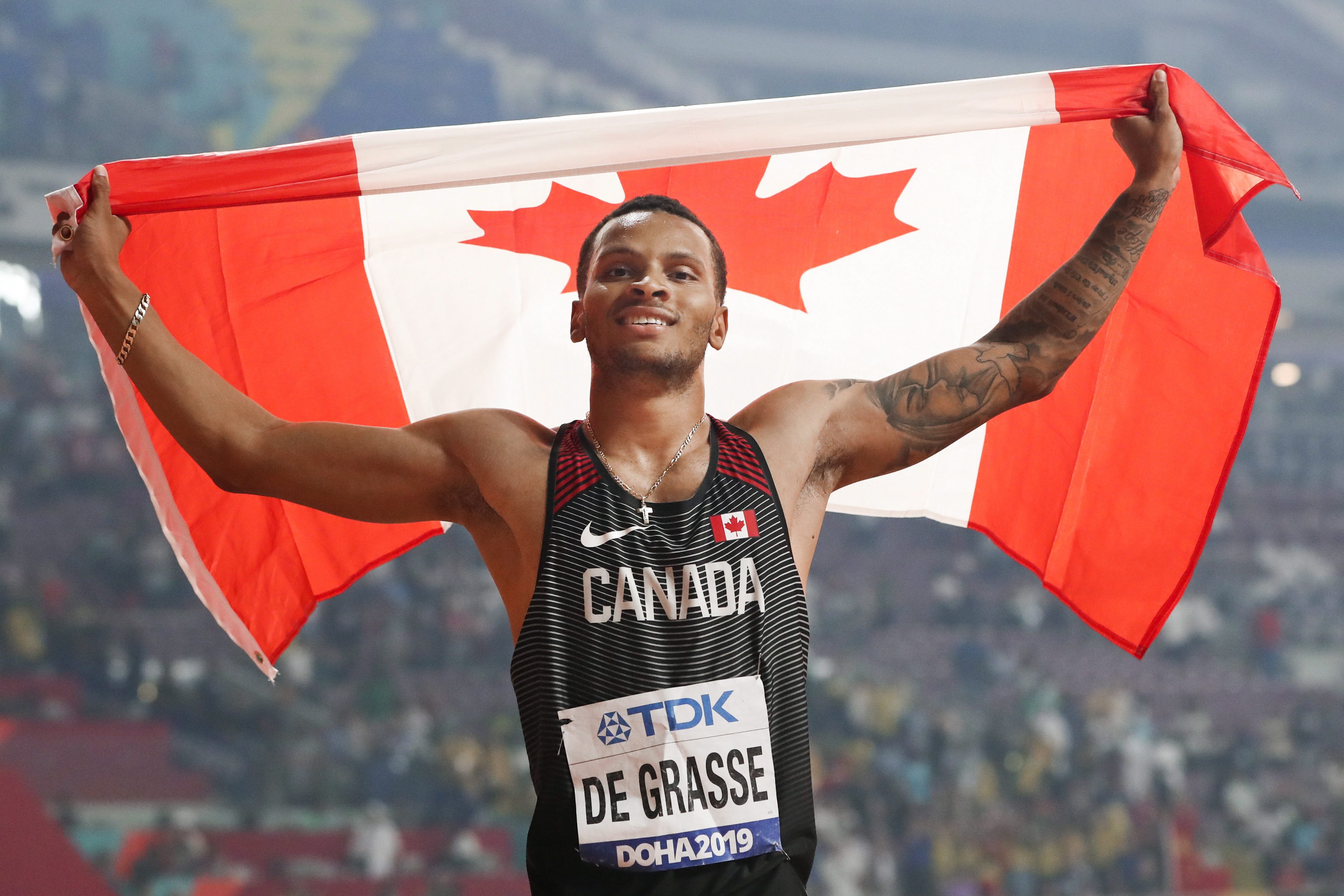 De Grasse holding Canadian flag above head smiling 