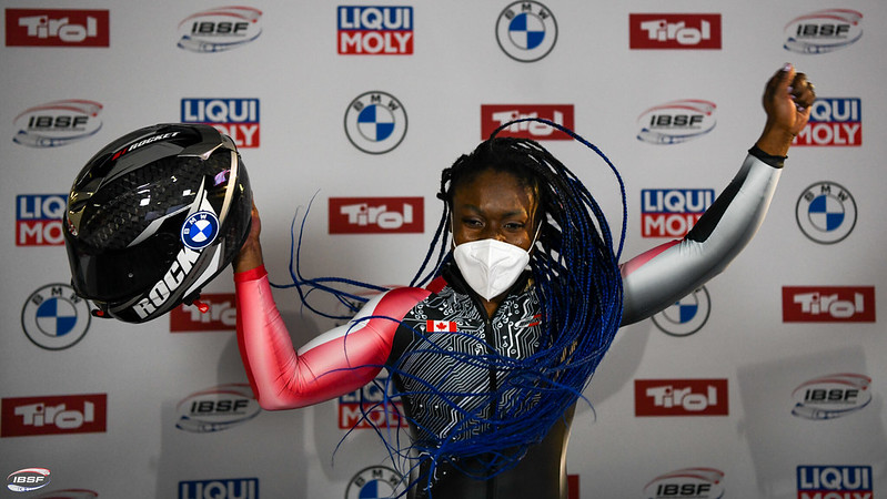 Cynthia Appiah raises her hands in the air, holding her helmet in her right hand.