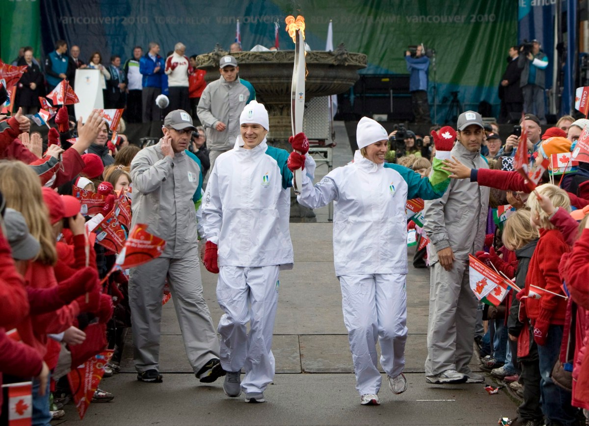 Two torchbearers run through a crowd holding the torch aloft