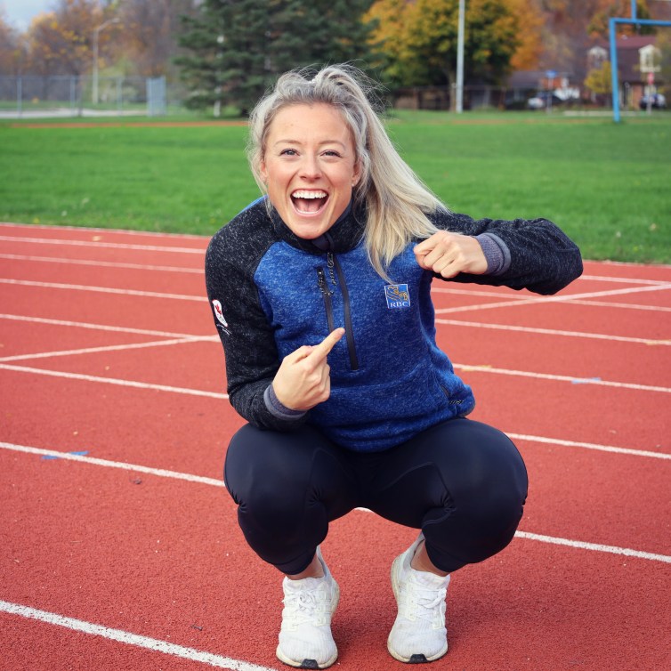 Kelsey Mitchell squatting on track pointing to RBC logo on her sweater