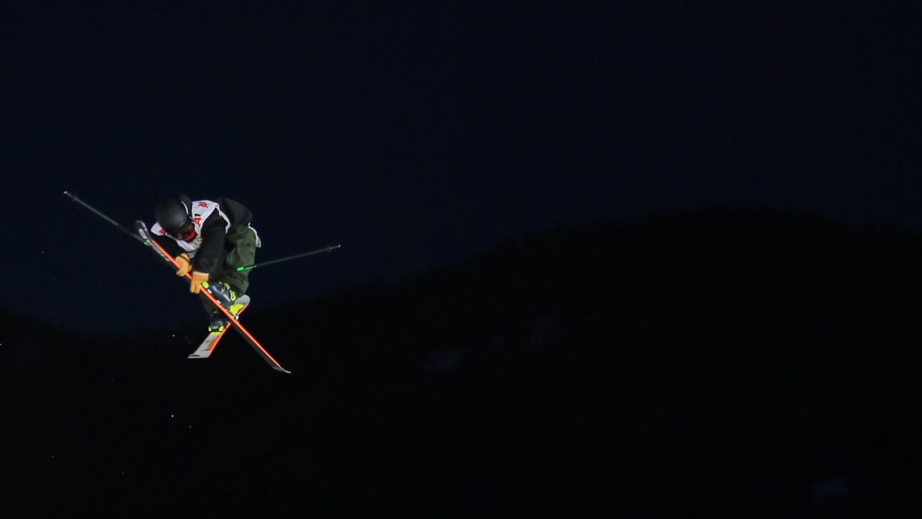 Edouard Therriault, a freestyle skier, mid-air during a run. The sky is dark.