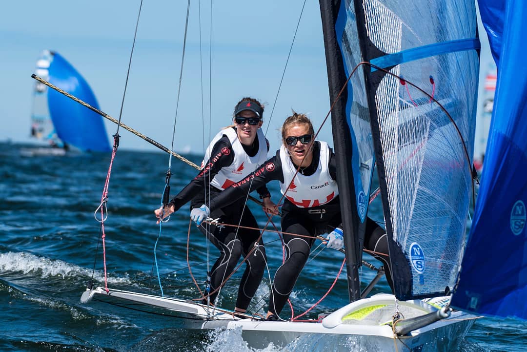 Two sailors standing on their boat pulling on rigging