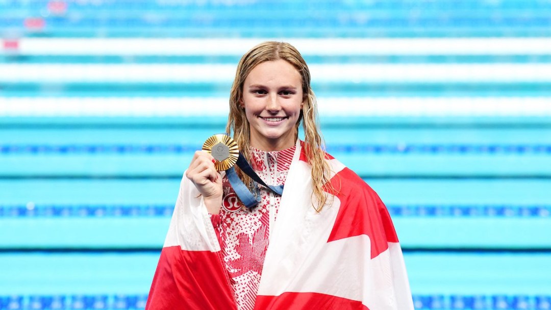 Summer McIntosh smiles with a Canada flag draped over her shoulders and holding her gold medal