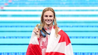 Summer McIntosh smiles with a Canada flag draped over her shoulders and holding her gold medal