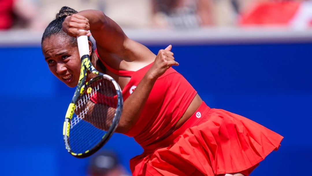 Leylah Fernandez hits a tennis ball while wearing an all red outfit in front of a blue background