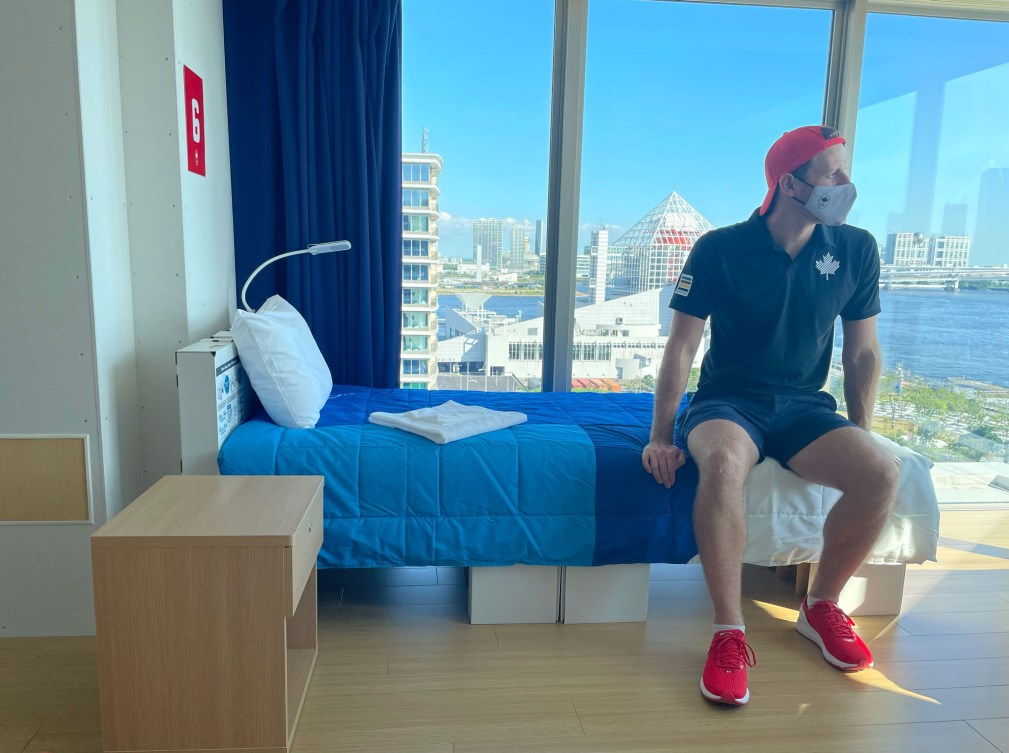Male athlete sits on cardboard bed in his room in Team Canada building