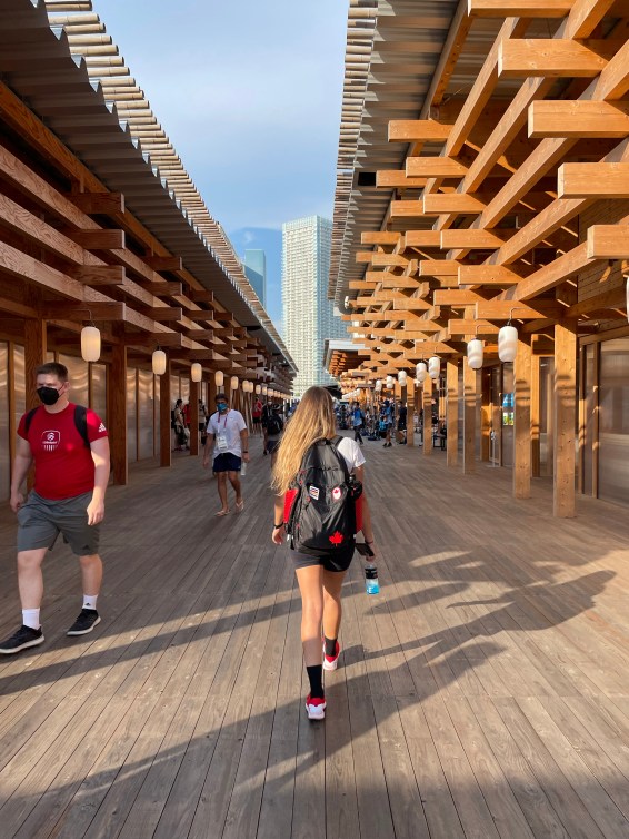 Athletes walk between buildings in the Olympic Village with the buildings created with wood larch