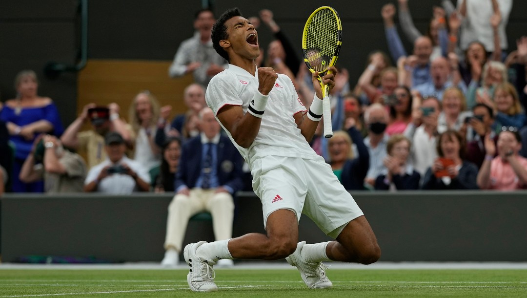 Felix kneels to the ground and pumps his arms in celebration after defeating Alexander Zverev. A out of focus crowd in the background.