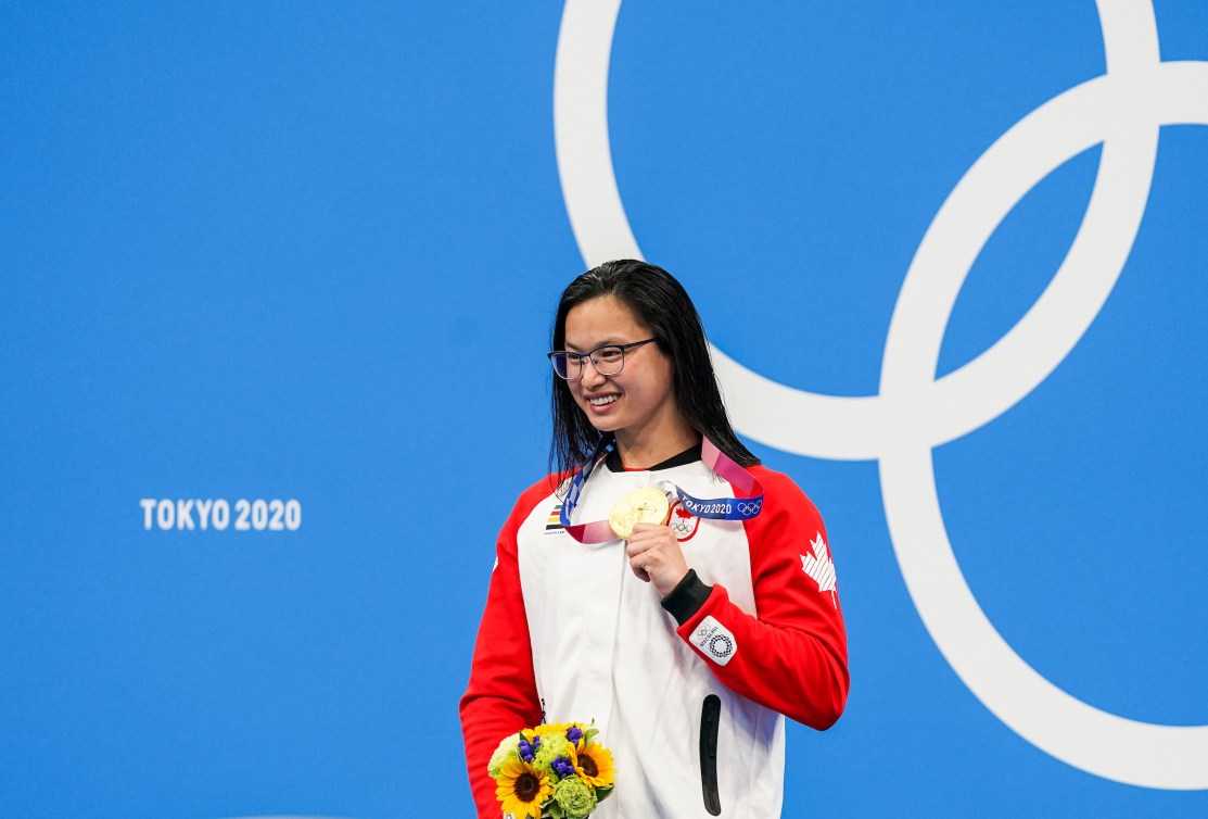 Maggie Mac Neil holds up gold medal on podium 