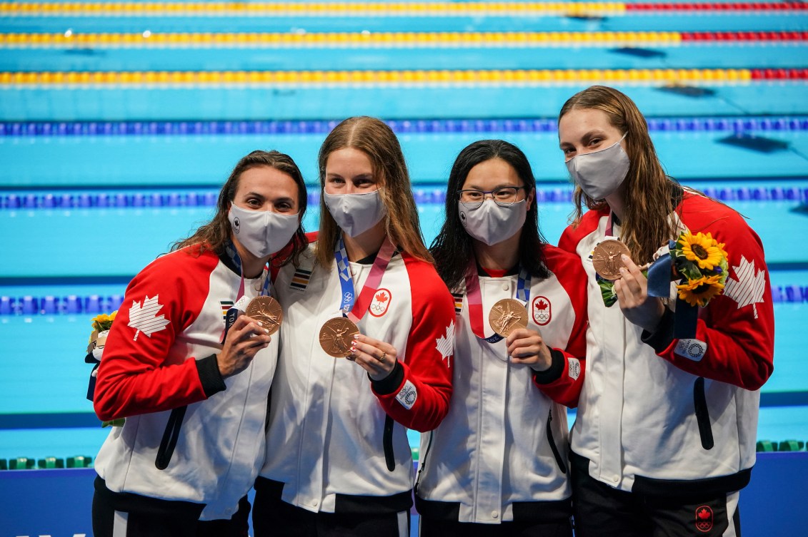 Canadian swimmers holding their bronze medals and flowers by the poolside