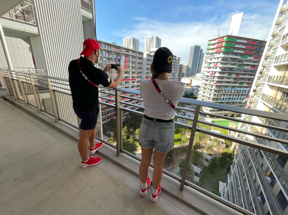 Male and female athlete stand on balcony overlooking views of athlete's village