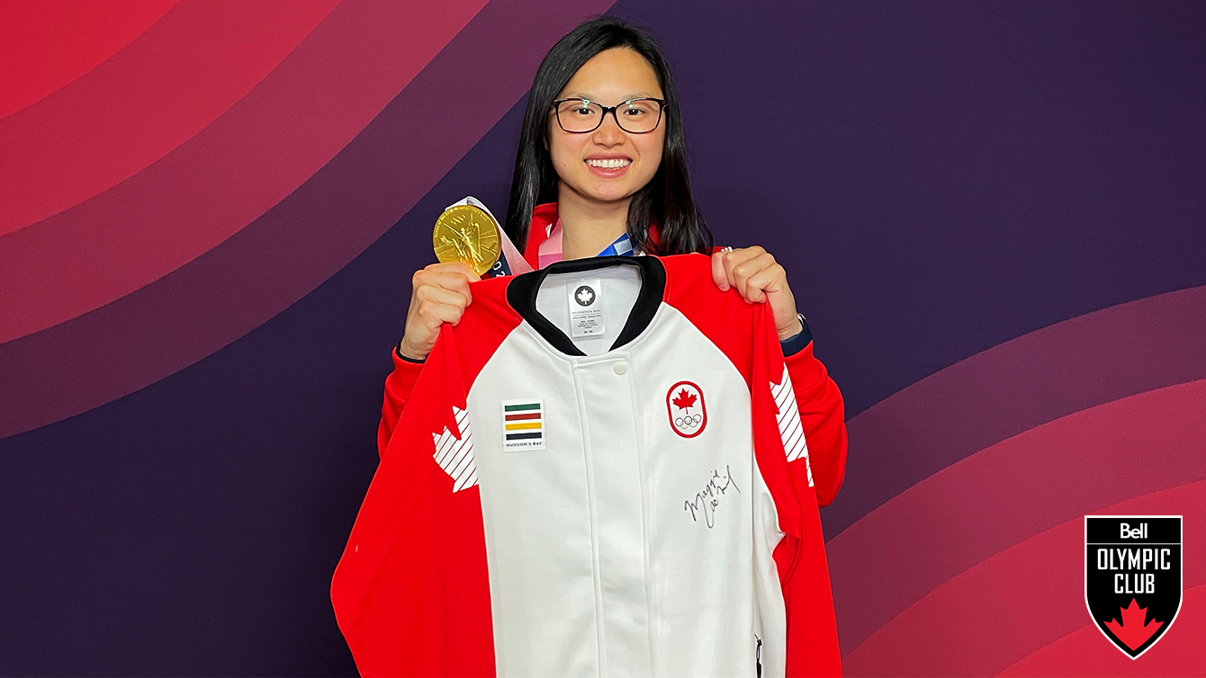 girl stands in front of red backdrop holding a white jacket and a gold medal