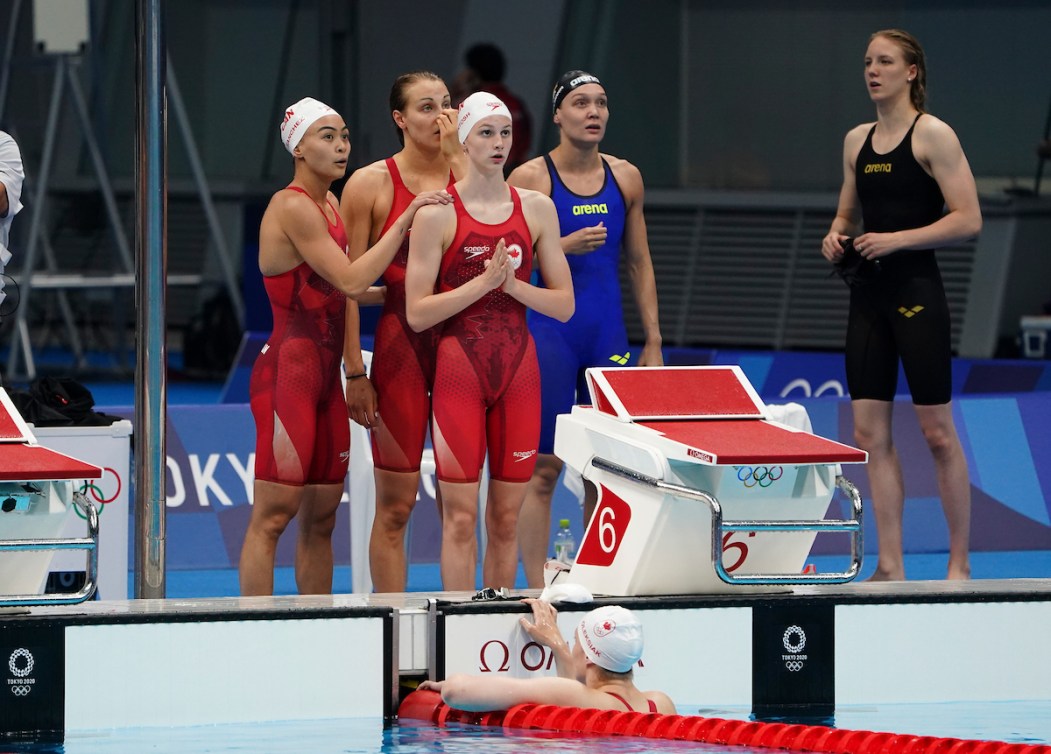 Canadian swimmers stand on the deck watching the score board