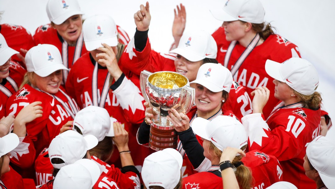 Marie-Philip Poulin holds up the trophy while surrounded by her teammates.