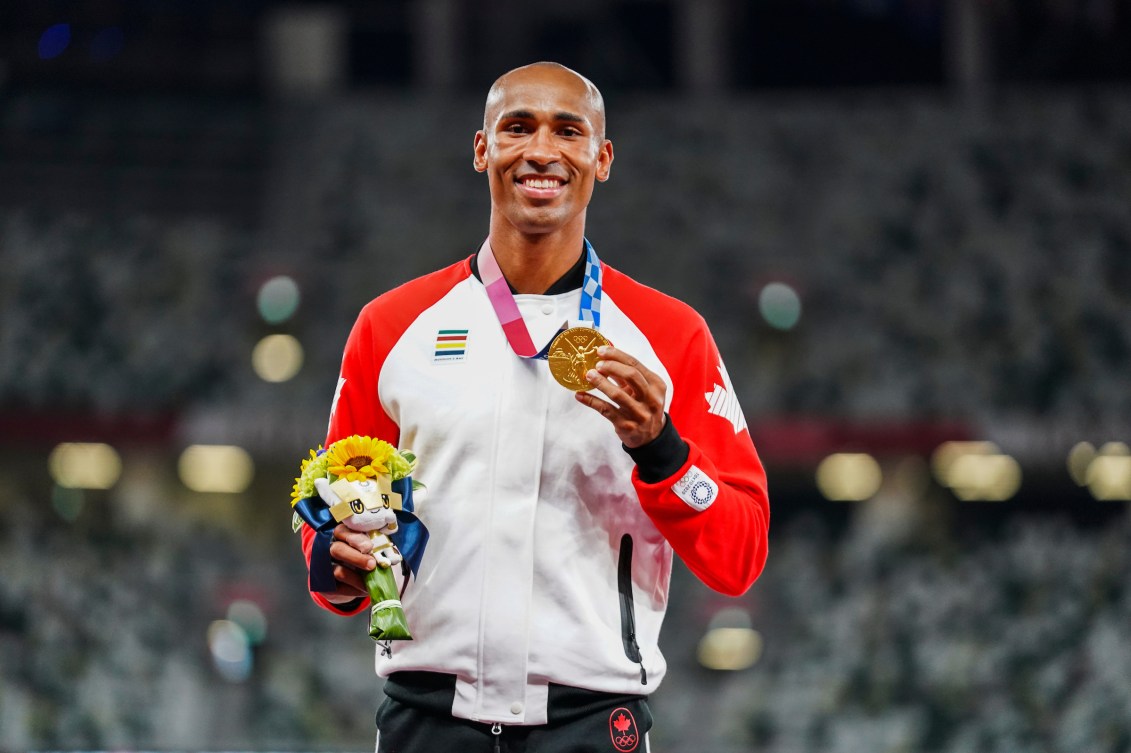 Damian Warner smiles on the podium wearing his gold medal 