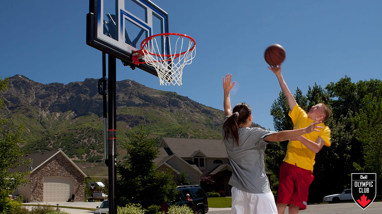 two teenagers play basketball on a driveway basketball net