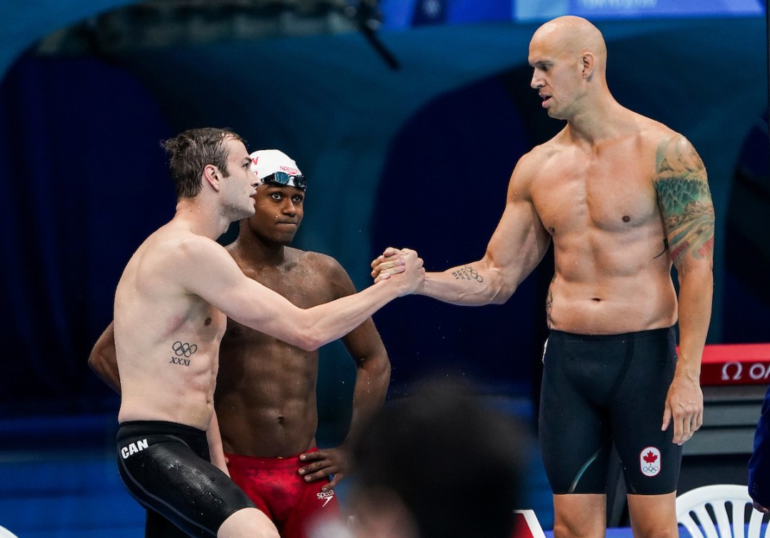Three male Canadian swimmers stand on the pool deck