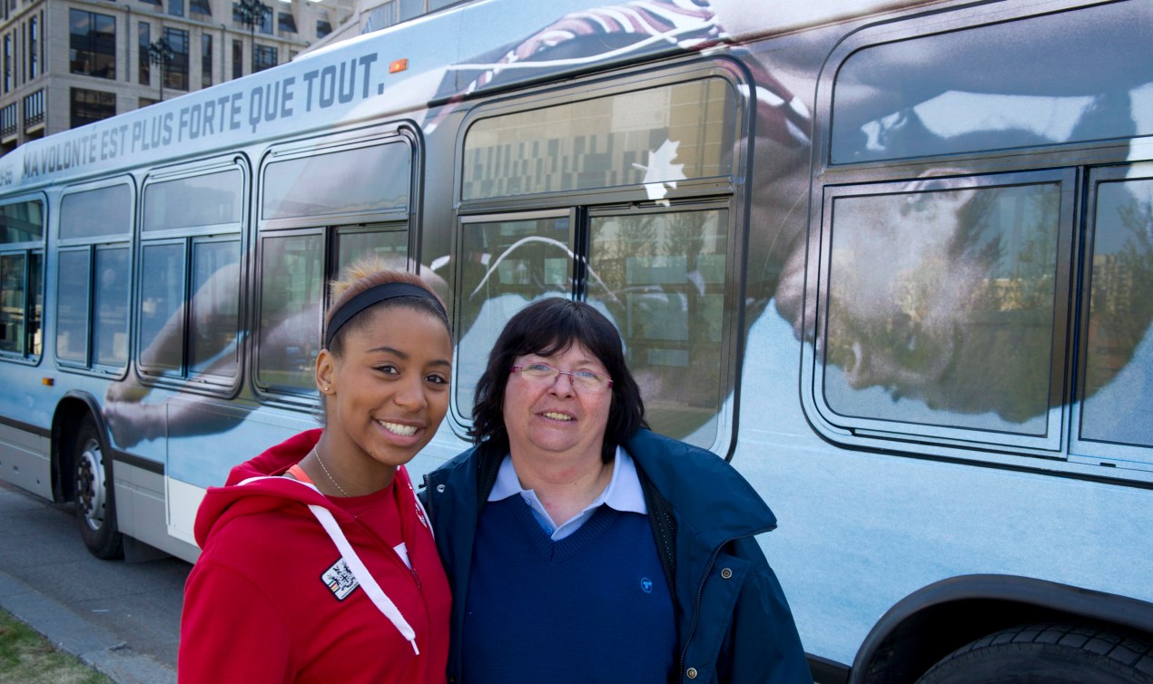 Jennifer Abel and her mother pose in front of a city bus with Abel's image on the side