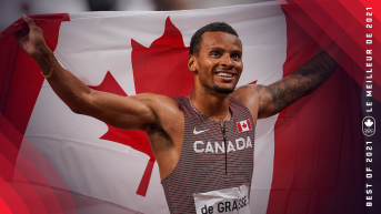 Andre De Grasse smiles as he holds a Canadian flag behind his back