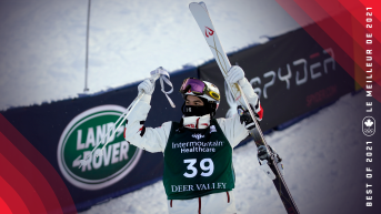 Mikael Kingsbury lifts his ski poles and skis above his head in celebration.
