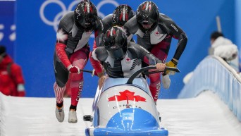 Four bobsledders jump into a sled at the start of a run
