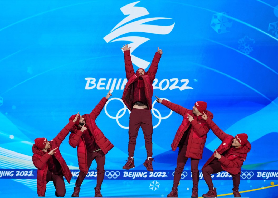 Teammates point at Charles Hamelin on the Olympic podium